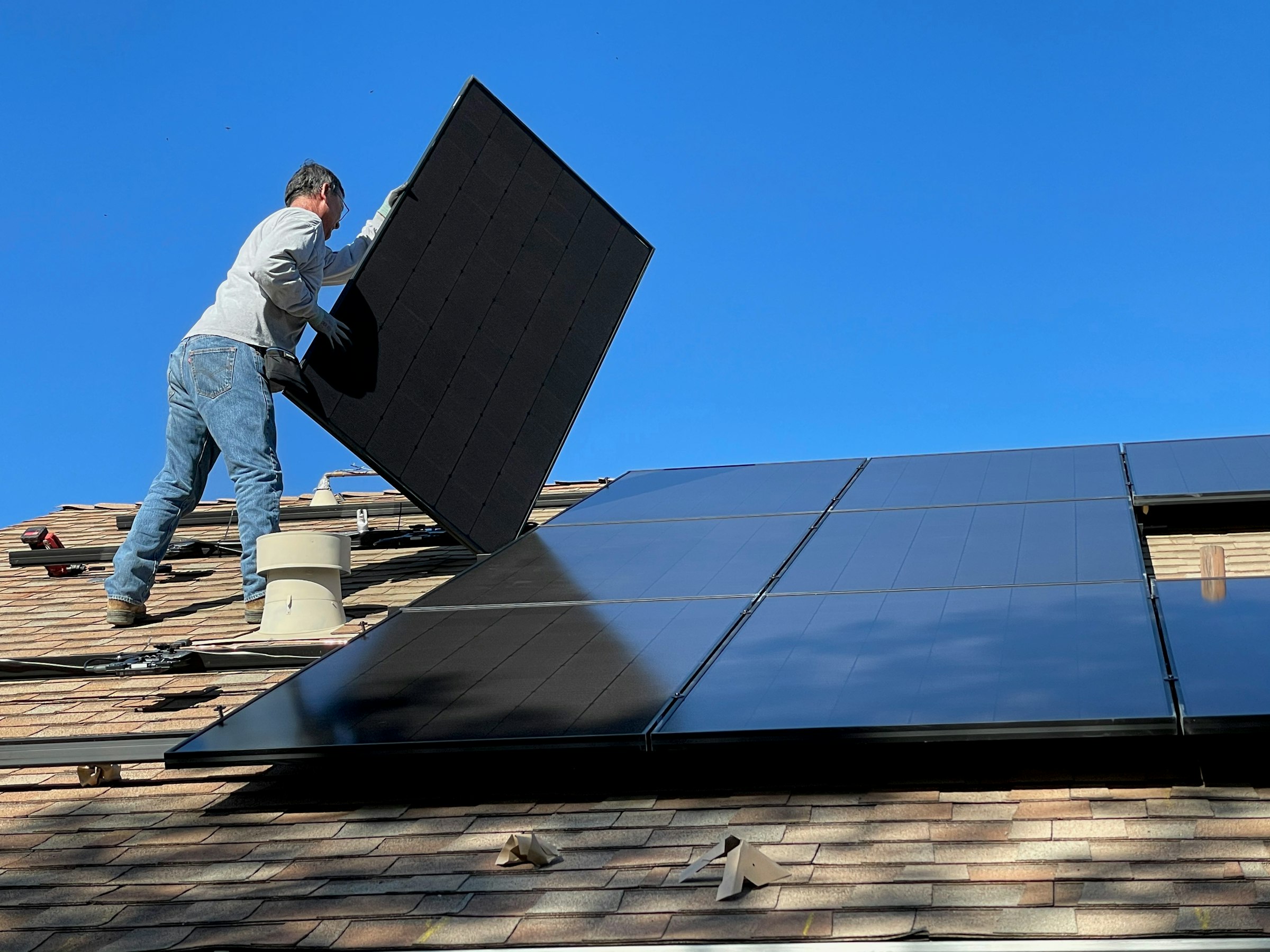 An installer setting a solar panel onto a residential roof array
